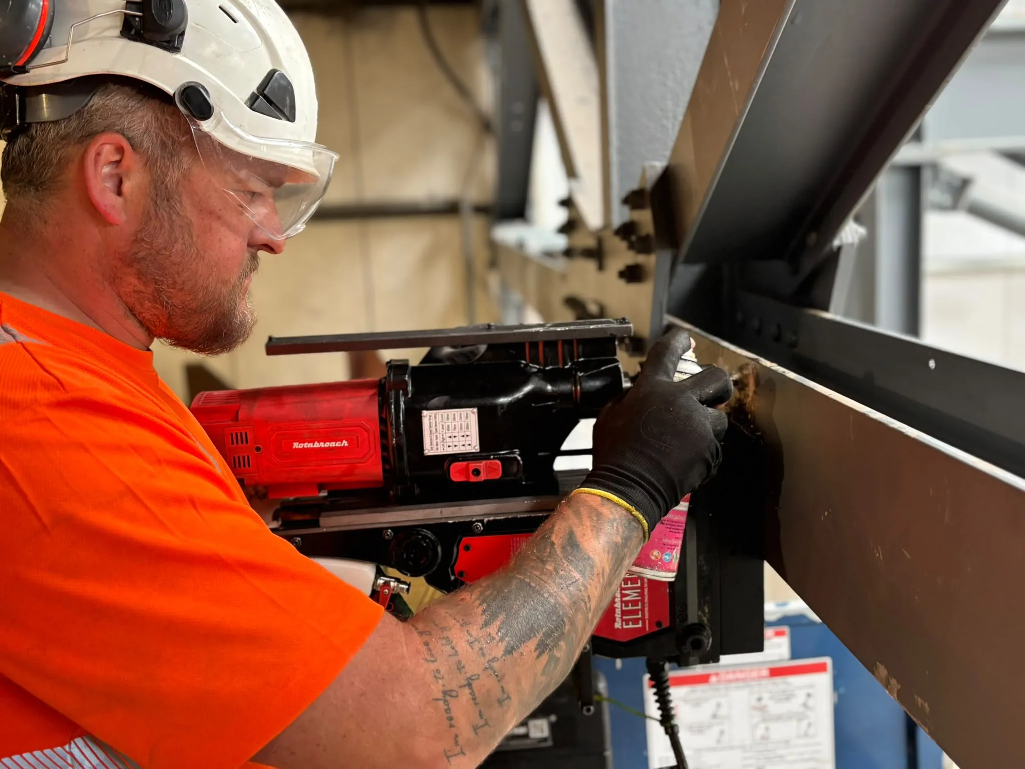 A Dawsons engineer in hard hat and safety glasses using a magnetic drill on structural steelwork