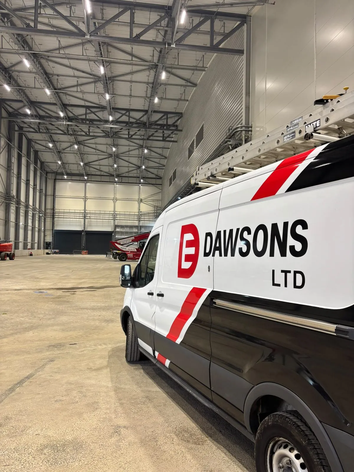 A liveried Dawsons Ltd van with roof ladders parked inside a large industrial building
