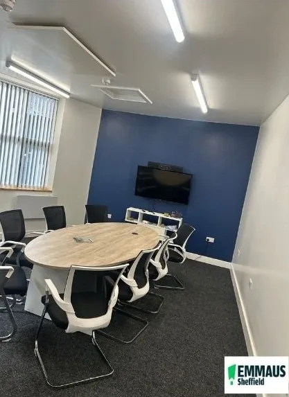 Meeting room with an oval table and chairs, a wall-mounted screen and a blue feature wall