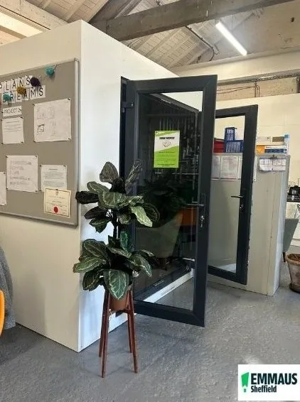 Office entrance with a glazed anthracite-framed door and screen, beside a noticeboard and a potted plant