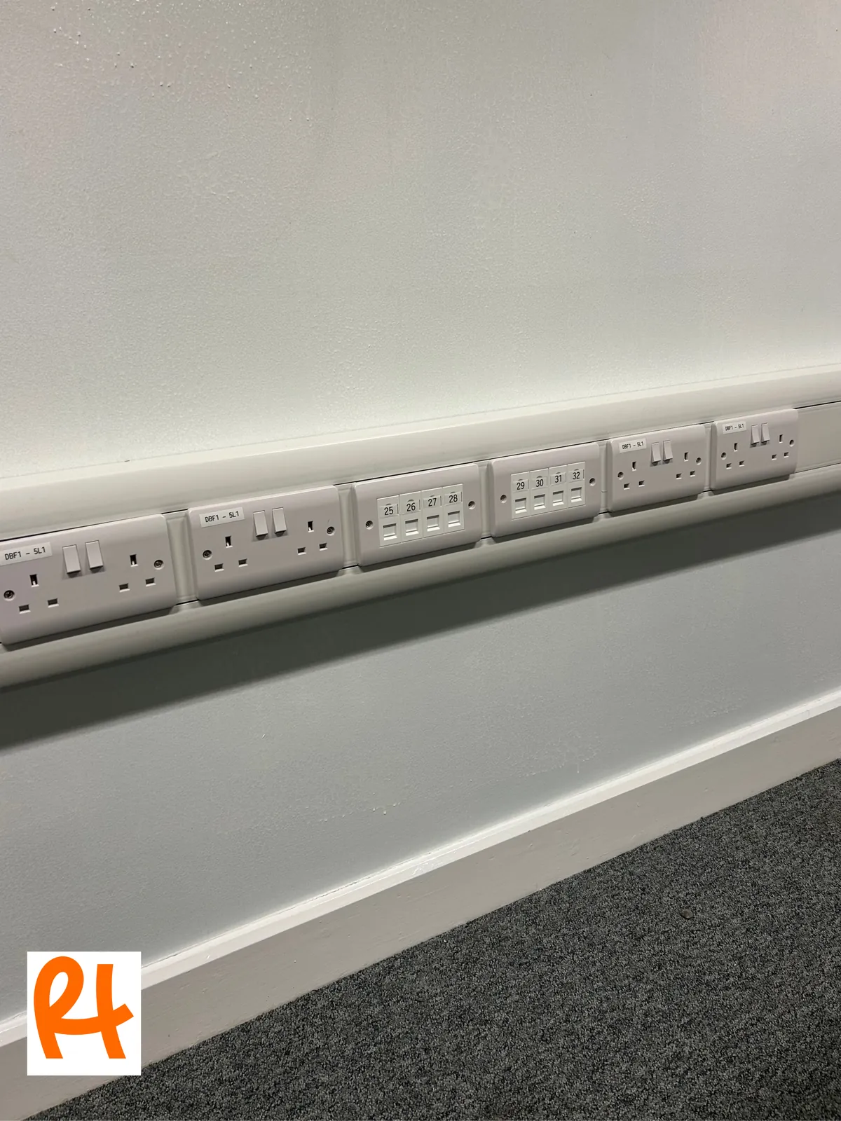 A run of newly installed, labelled power sockets and network outlets in white dado trunking